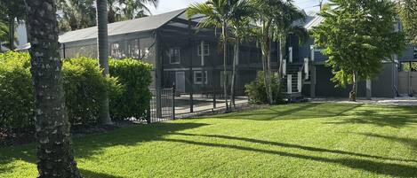 A residential area with a well-maintained lawn, a house with a large balcony, and a clear sky.