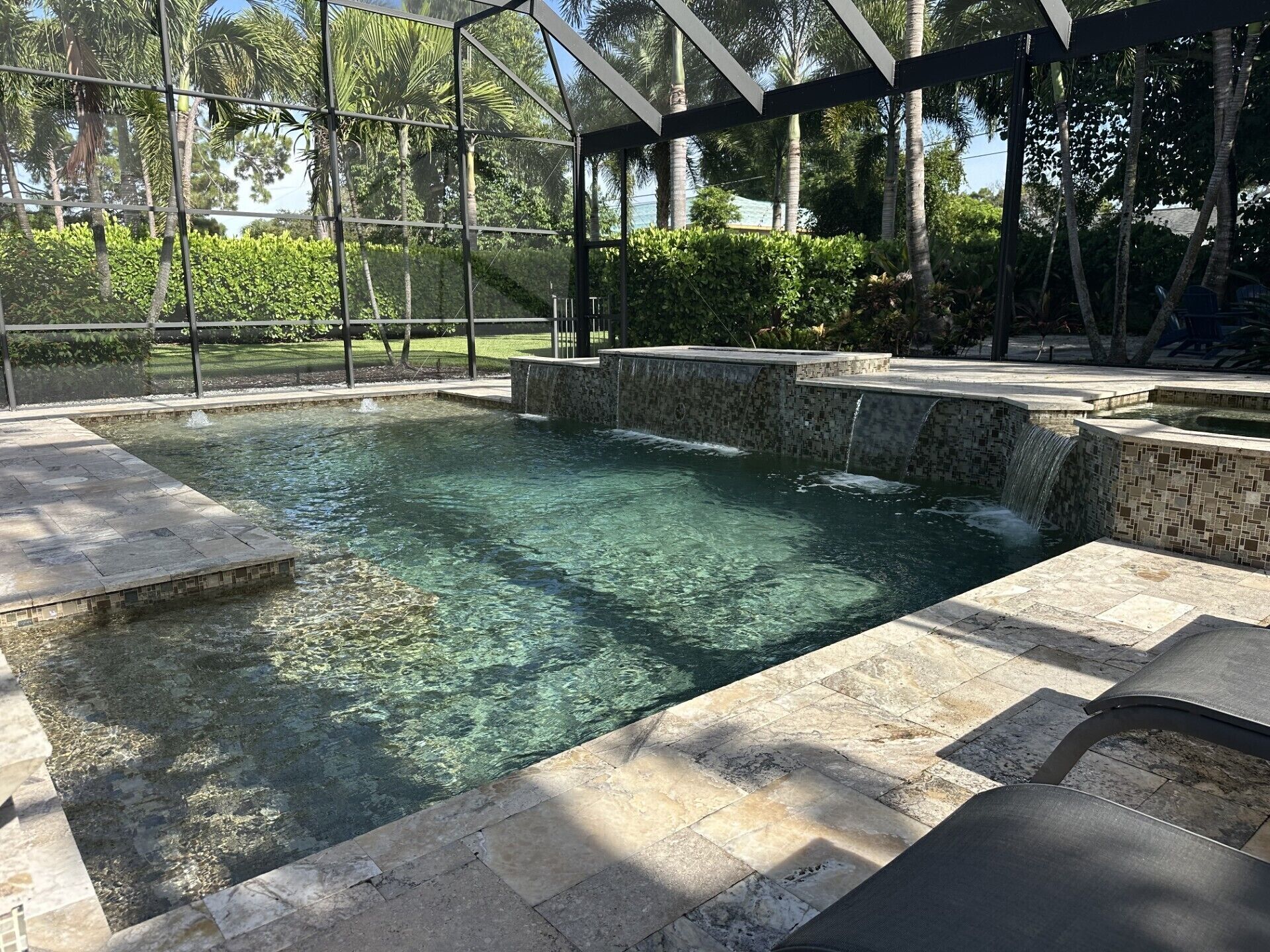 A clear swimming pool with a tiled deck, surrounded by a covered area with a metal frame and glass panels.