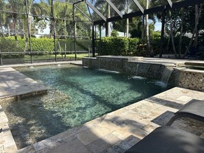 A clear swimming pool with a tiled deck, surrounded by a covered area with a metal frame and glass panels.