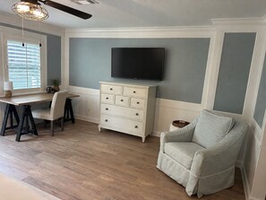 A room with a desk, chair, television, and a sofa.