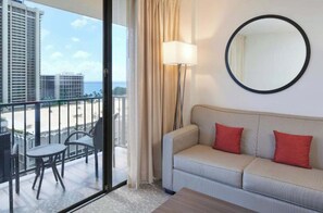 A hotel room with a balcony, a sofa, a round mirror, and a lamp. - Waikiki Escape Steps from the Beach (Honolulu)