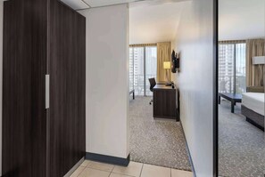 Ein Hotelzimmer mit einem dunklen Holzschrank, einem Schreibtisch mit Stuhl, einem Bett und einem großen Fenster mit Vorhängen.