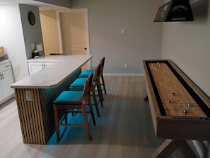 A kitchen with a bar area, wooden stools, a foosball table, and a clock on the wall.
