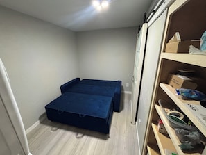 A room with a bed, a wardrobe, and a shelf with various items.