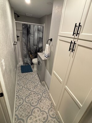 A bathroom with a toilet, a sink, a towel rack, patterned floor tiles, and a shower curtain. - Boji Park Shuffle: 5-bedroom home in the middle of all the action (Arnolds Park)