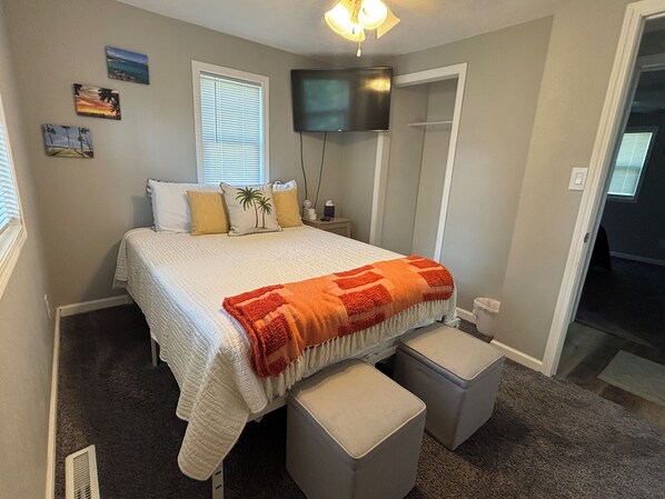 A bedroom with a bed, a TV, a window, and a door.