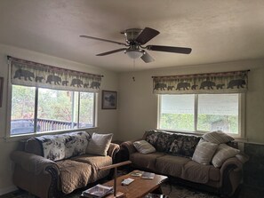 A living room with two sofas, a ceiling fan, and windows with curtains.