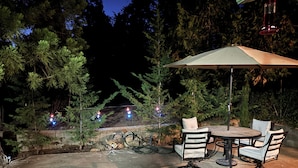An outdoor patio with a round table and chairs, surrounded by trees and a stone wall.