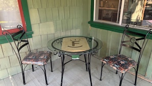 A glass-top table with two chairs, a wooden floor, and a window with a view of a kitchen.
