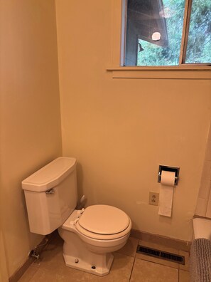 A standard bathroom with a toilet, a paper towel dispenser, and a window.
