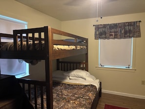 A bunk bed with a patterned bedspread, a window with curtains, and a ceiling light fixture.