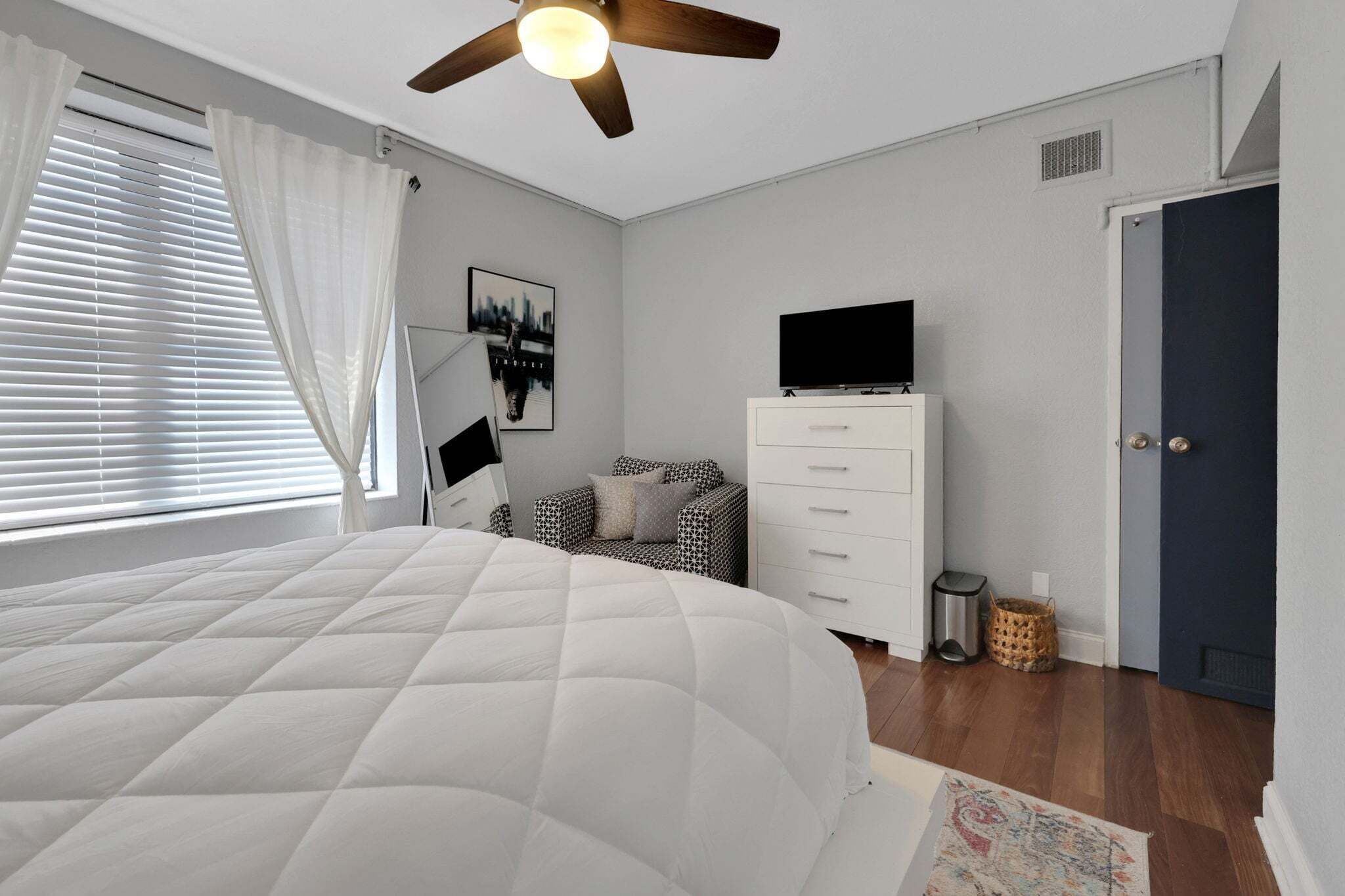 Une chambre à coucher avec un lit, une commode, un téléviseur et une porte.