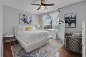 Um quarto moderno com cama, mesa de cabeceira, poltrona, ventoinha no teto e obras de arte nas paredes.