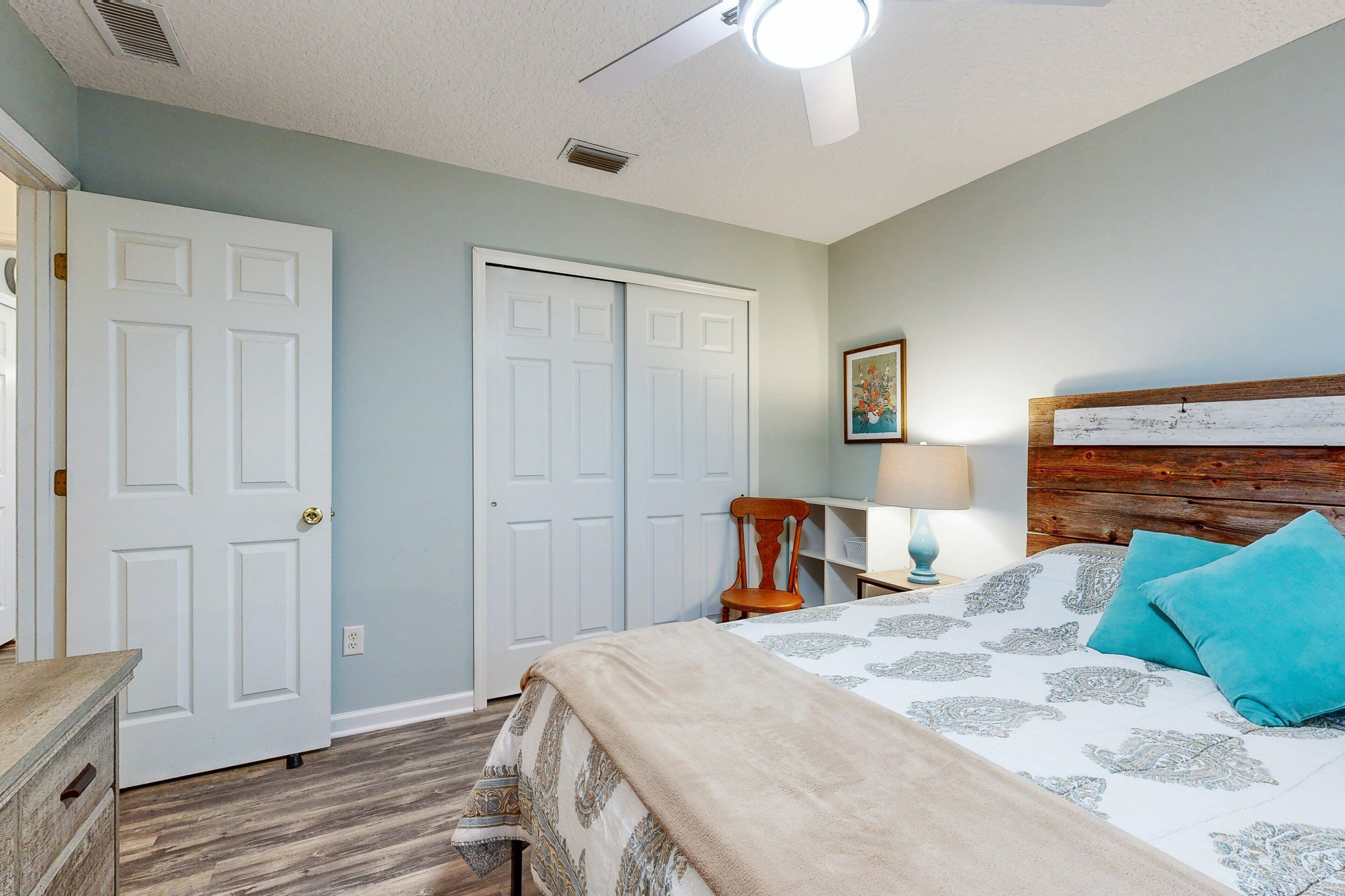A bedroom with a bed, a nightstand, a chair, a lamp, and a ceiling fan.