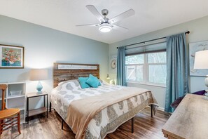 A bedroom with a bed, a nightstand, a chair, a desk, a ceiling fan, and a window with curtains. - Breezy Bungalow Near Beach/golf With Private Patio & Updated Interior (Fernandina Beach)