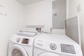 A laundry area with a washing machine and dryer, a small shelf, and a mirror. - Delightful Condo in Gated Community With Ocean Views, Balcony, AC & Pool (Fernandina Beach)