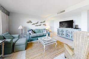 A living room with a sectional sofa, a coffee table, a TV, and a cabinet with glass doors. - Delightful Condo in Gated Community With Ocean Views, Balcony, AC & Pool (Fernandina Beach)