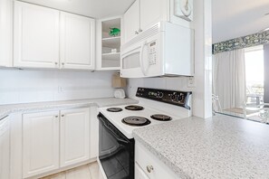 A kitchen with white cabinets, a stove, and a microwave. - Delightful Condo in Gated Community With Ocean Views, Balcony, AC & Pool (Fernandina Beach)