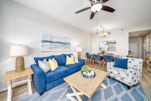 A living room with a blue sofa, a patterned armchair, a coffee table, and a ceiling fan. - Coastal Luxury at Surf Club Direct Oceanfront Resort-style Amenities (Palm Coast)