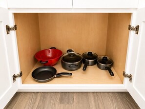 A kitchen cabinet with a wooden interior, containing a red colander, a black frying pan, and three black pots.
