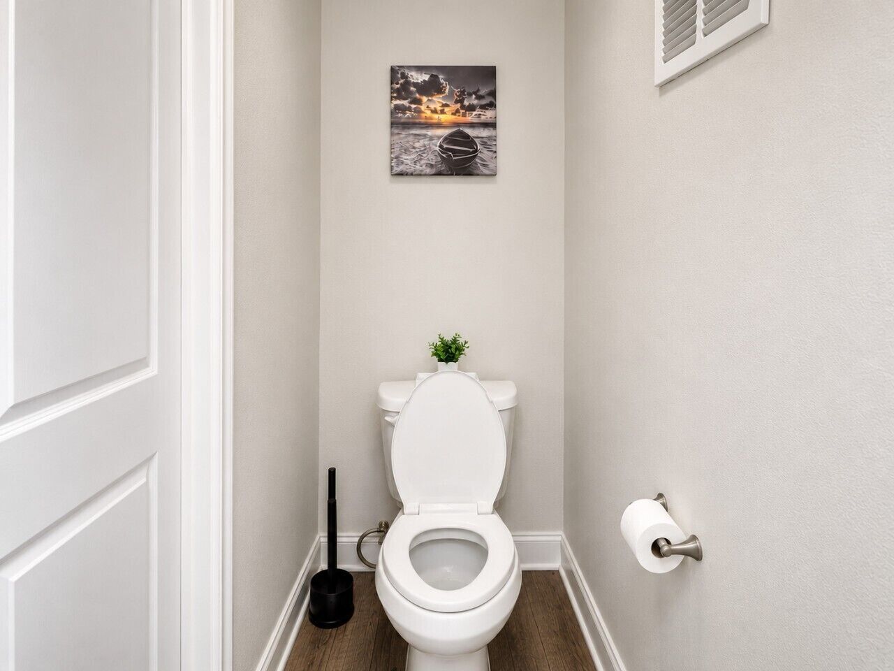 Een badkamer met een wit toilet, een klein plantje op de tank, een zuiger en een toiletrolhouder.