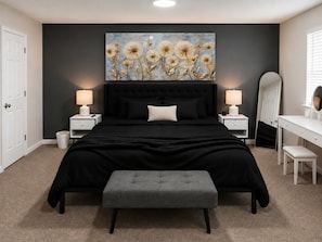 Une chambre à coucher avec un grand lit, des tables de chevet, un banc, une commode et un miroir.
