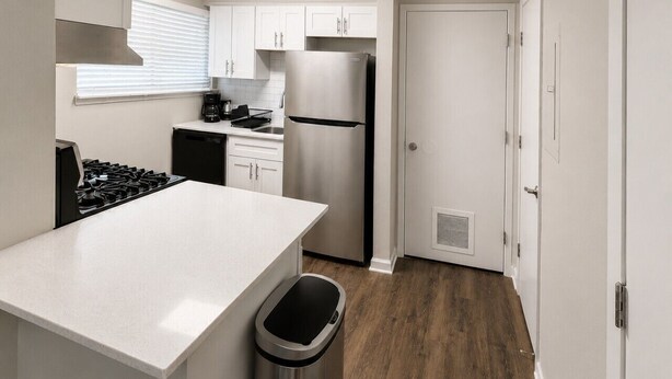 A modern kitchen with white cabinets, a stainless steel refrigerator, and a black trash bin.