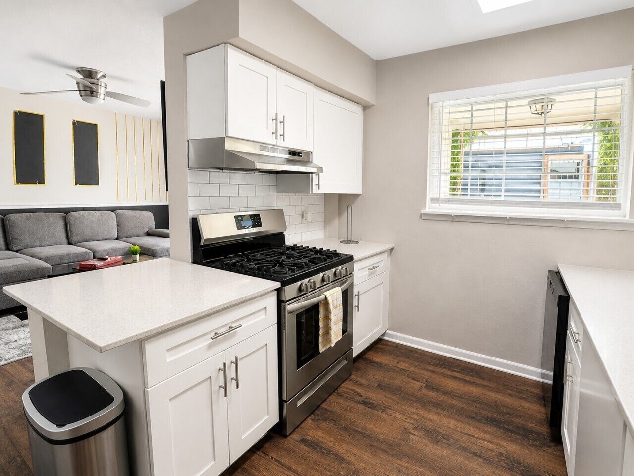 A modern kitchen with white cabinetry, a stainless steel stove, and a window with blinds.