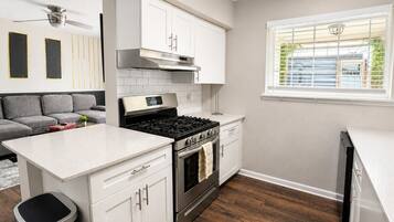 A modern kitchen with white cabinetry, a stainless steel stove, and a window with blinds.