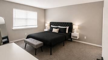 A bedroom with a bed, bedside tables, a bench, a mirror, and a window with blinds.