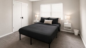 Een slaapkamer met een bed, nachtkastjes, een raam met zonwering, een deur en een vloerbedekking.