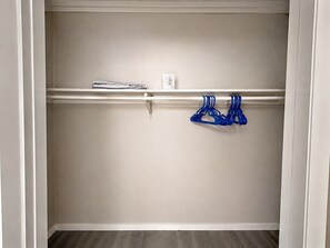 A closet with a white door, a shelf with folded clothes, and a blue hanger on a rod.