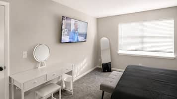 Un dormitorio con una cama, un escritorio con espejo, una televisión y una ventana con persianas.