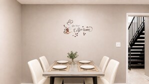 Een eetkamer met een tafel gedekt voor vier personen, een decoratief bord aan de muur en een trap op de achtergrond.
