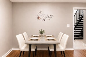 A dining room with a table set for four, a decorative wall sign, and a staircase in the background. - Modern Hoover Retreat | King + Queen (Hoover)