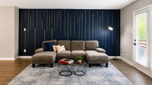 Een modulaire bank, een wand met een geometrisch ontwerp, een getextureerd vloerkleed en een klein bijzettafeltje met een plant.