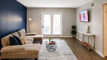A living room with a sofa set, a coffee table, a TV, and a door with a view.
