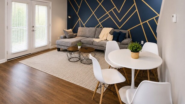 Ein Wohnzimmer mit einer Couch, Couchtisch und Stühlen, ein Essbereich mit Tisch und Stühlen und einer Wand mit geometrischem Muster.