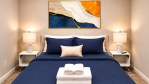 Ein Hotelzimmer mit einem großen Bett, zwei Nachttischlampen, einem Wandbild und einem Stapel Handtüchern auf dem Bett.