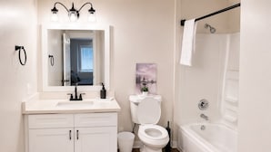Ein Badezimmer mit einem weißen Waschbecken, einer Toilette und einer Badewanne, einem Spiegel über dem Waschbecken und einem Bild an der Wand.