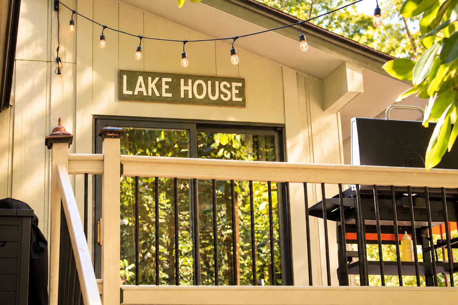 Une terrasse en bois avec une pancarte indiquant « MAISON AU BORD DU LAC » et un barbecue fixé à la rambarde.