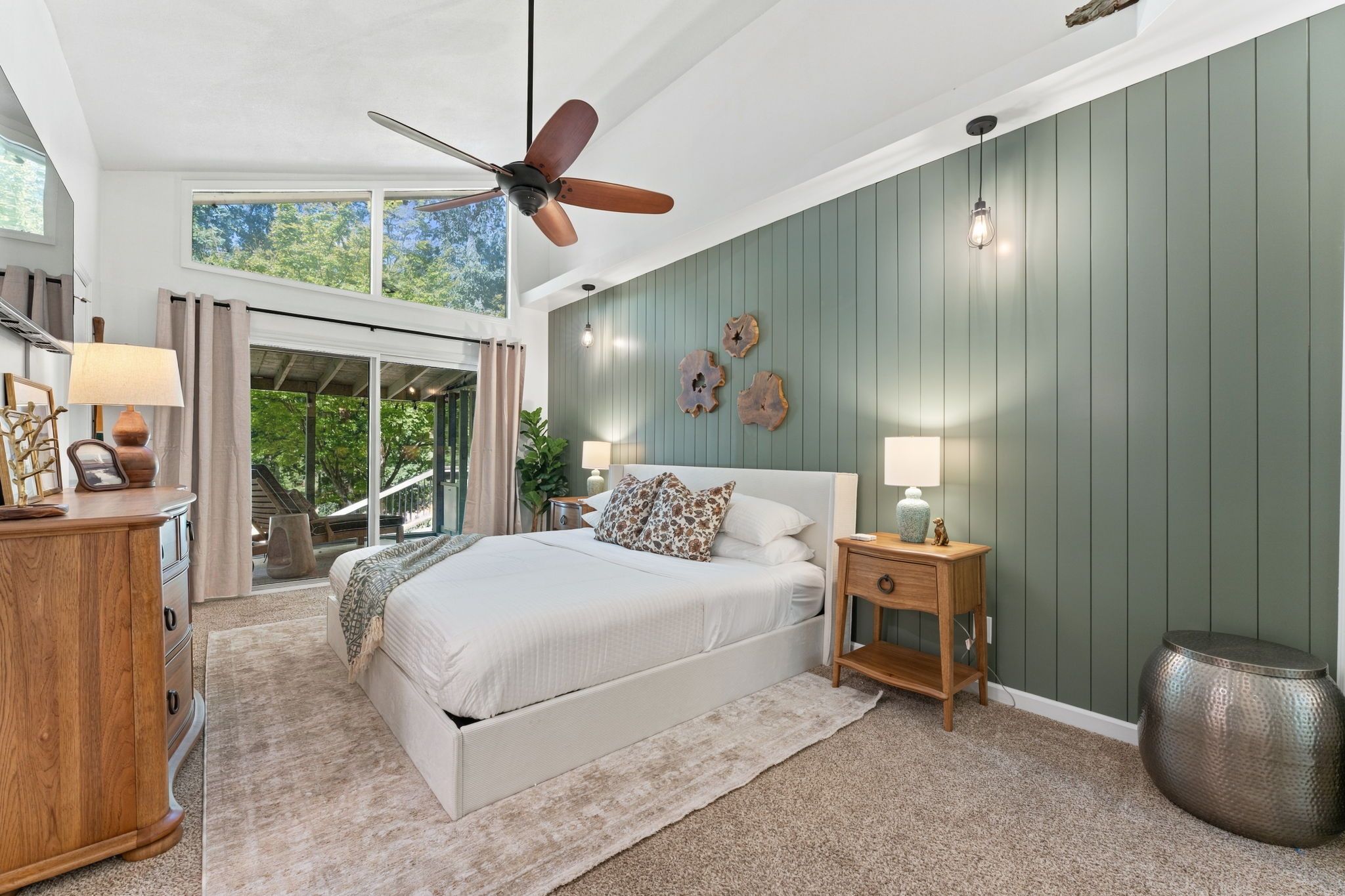 Un dormitorio con cama, mesita de noche, ventilador de techo y vista al exterior.