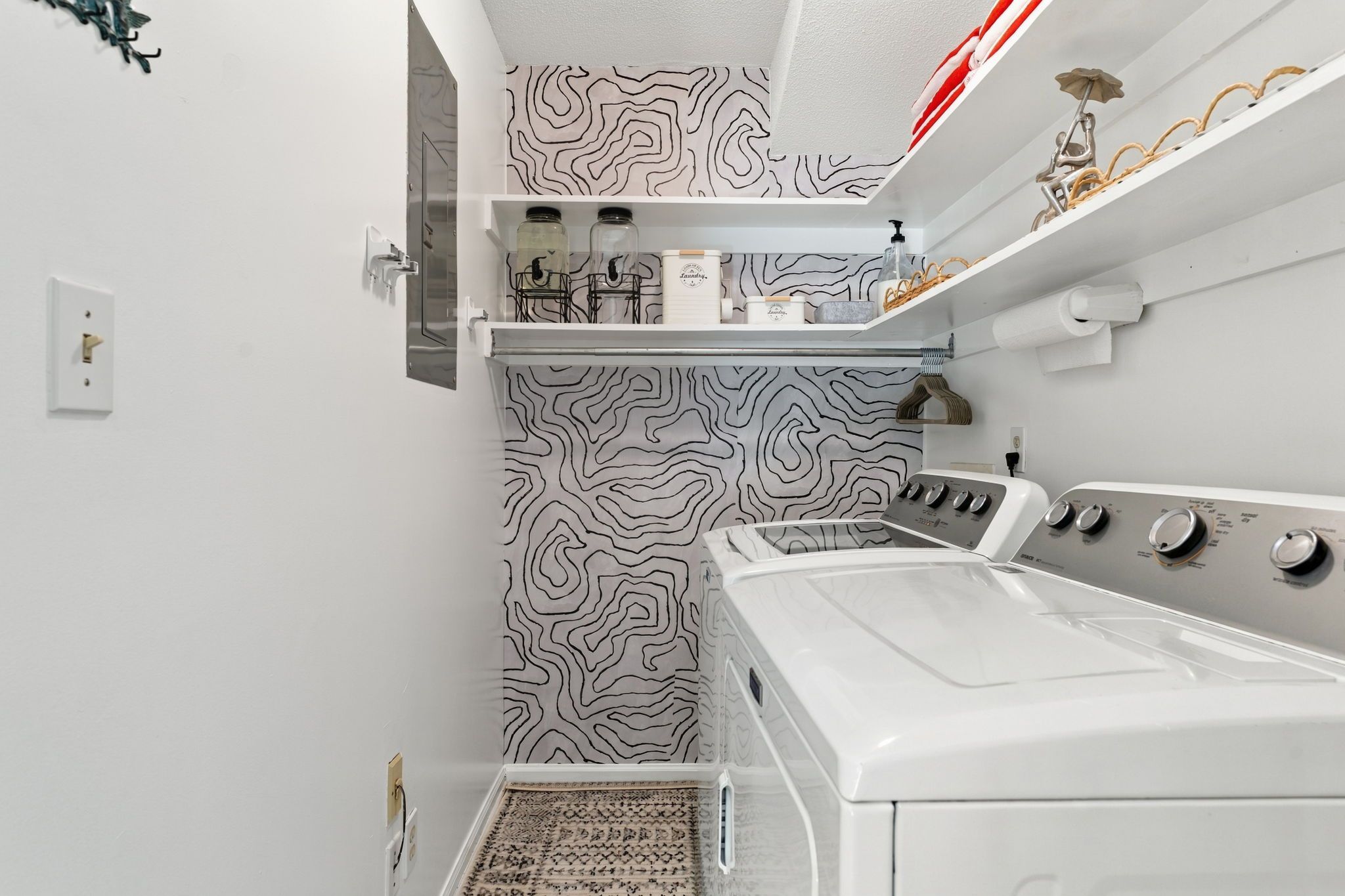 Un espacio pequeño para la lavandería con lavadora blanca, tendedero y papel tapiz estampado.