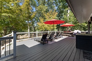 A wooden deck with outdoor seating, including lounge chairs and a table, under a covered area with red umbrellas.