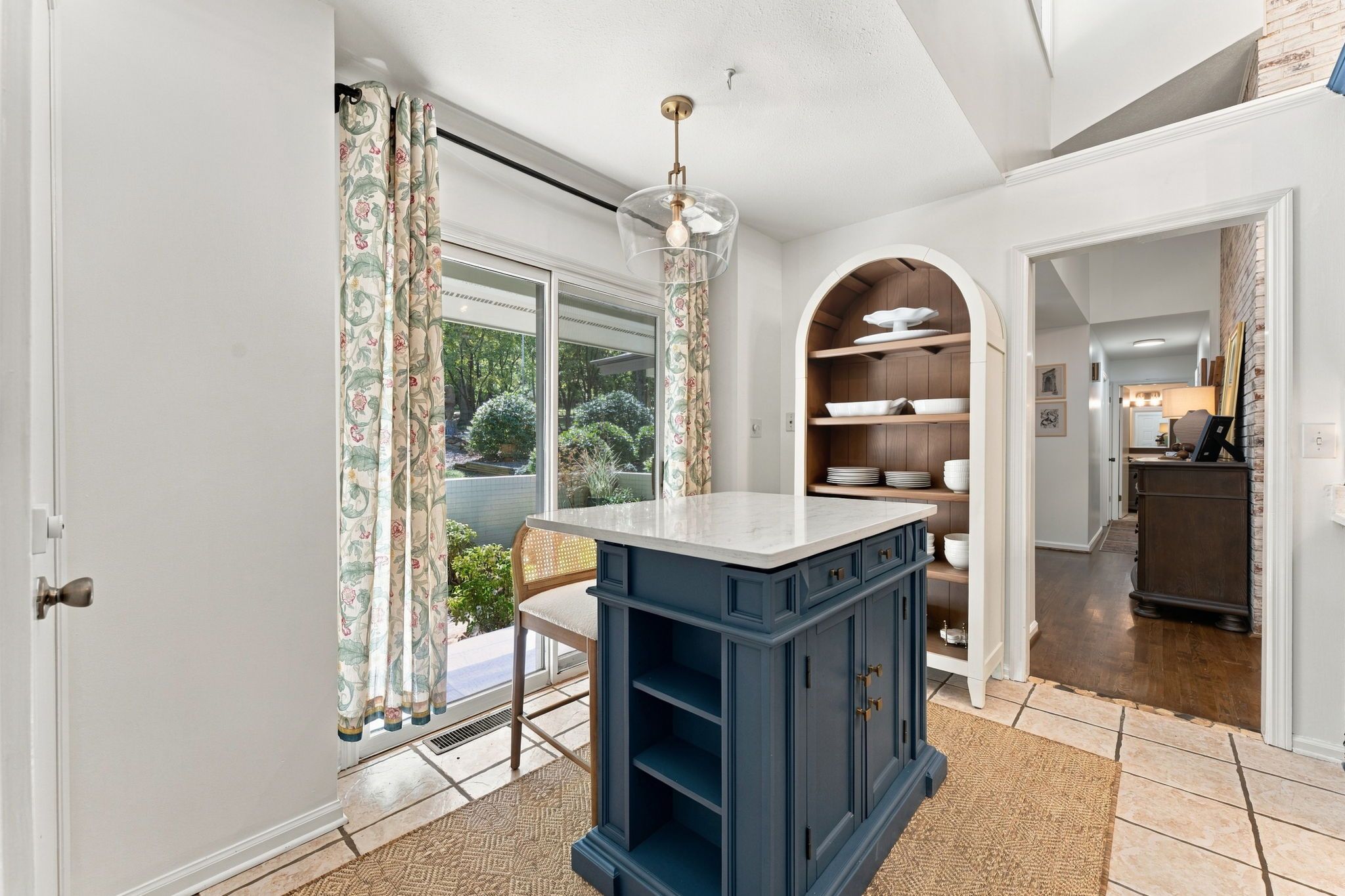 A kitchen with a marble countertop, a built-in shelf unit, and a view of the outdoors through a sliding glass door.