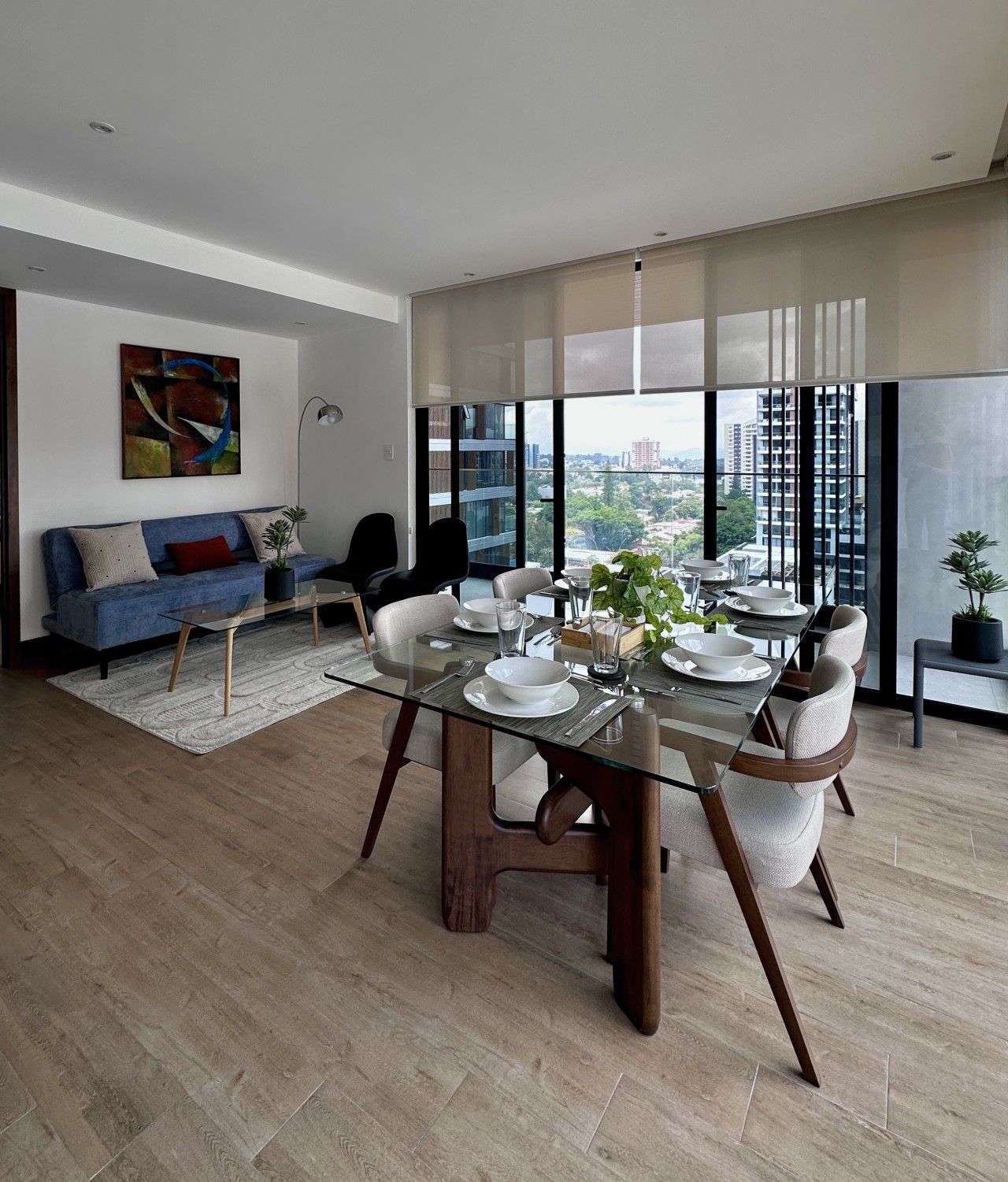 Un espace repas moderne avec une table en verre, des chaises et une vue sur la ville grâce à de grandes fenêtres.