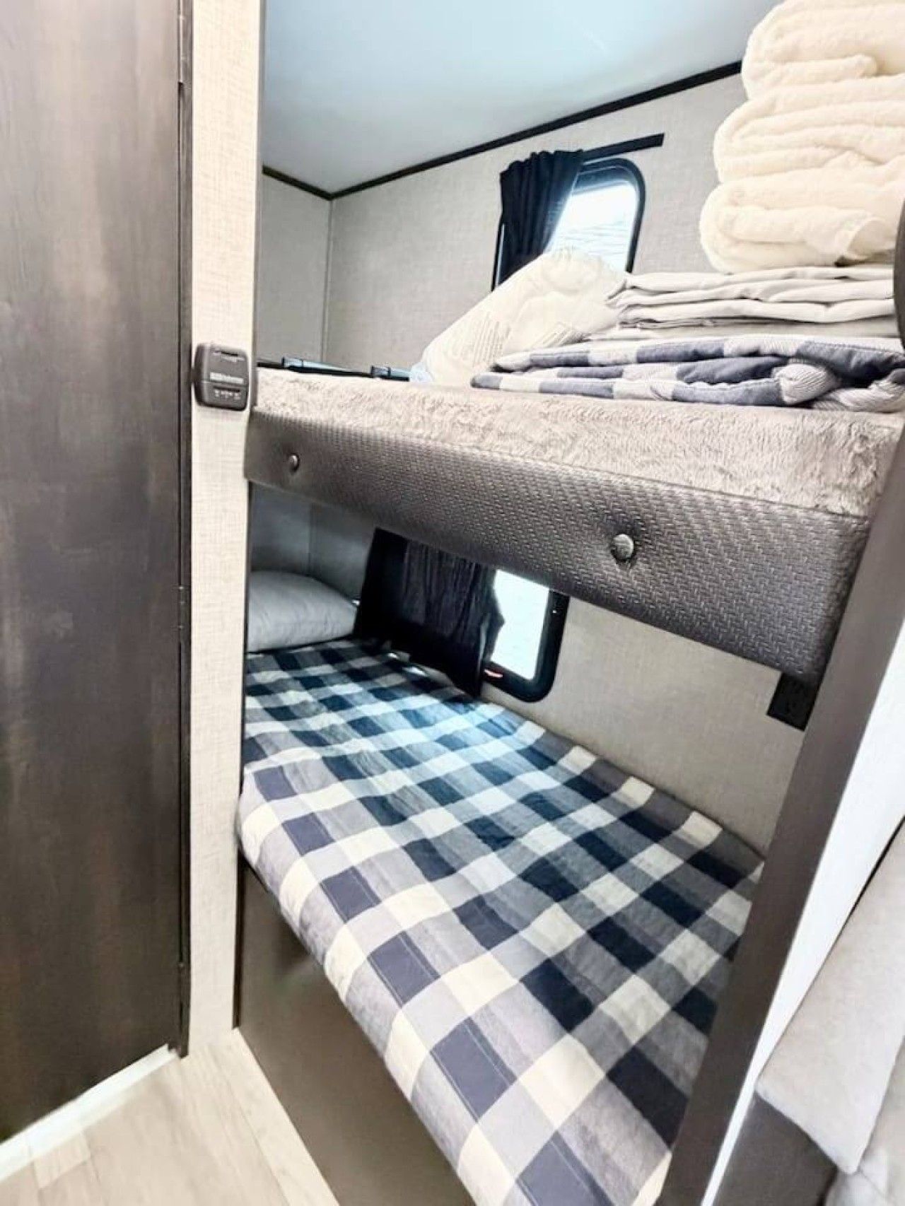 A compact RV interior with a bunk bed, a small window, and a checkered floor.