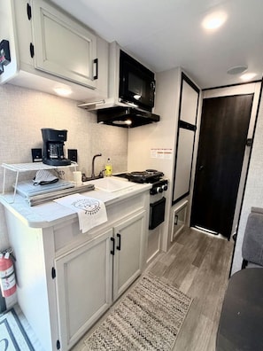 A compact kitchenette with a microwave, coffee maker, and stove. - Downtown New RV | 2 Blocks to Momentary & Trails (Bentonville)
