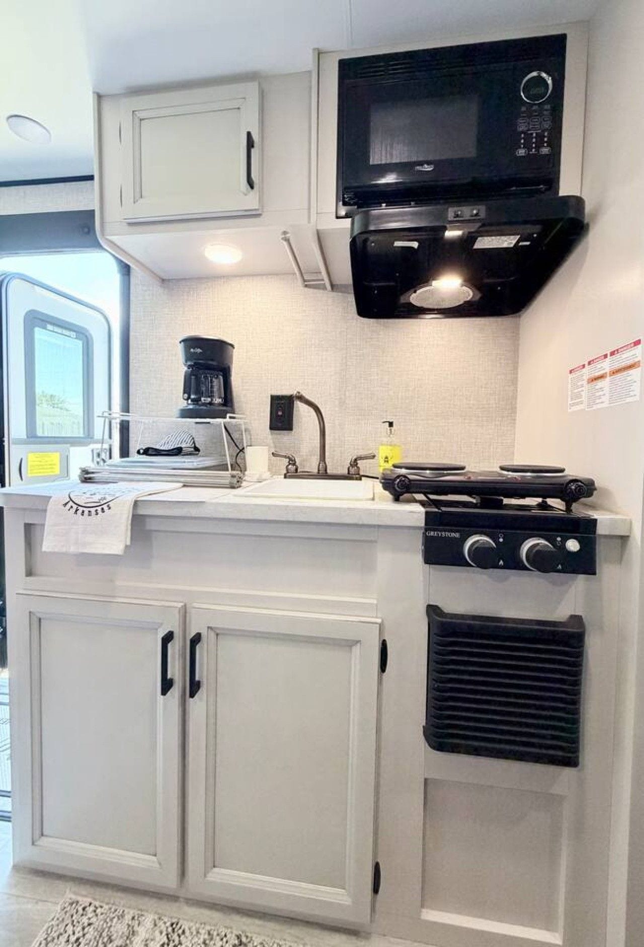 A compact kitchen with a microwave, coffee maker, and a gas stove.