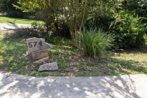 A stone sign with the number 574 in a landscaped area with grass, shrubs, and a tree.